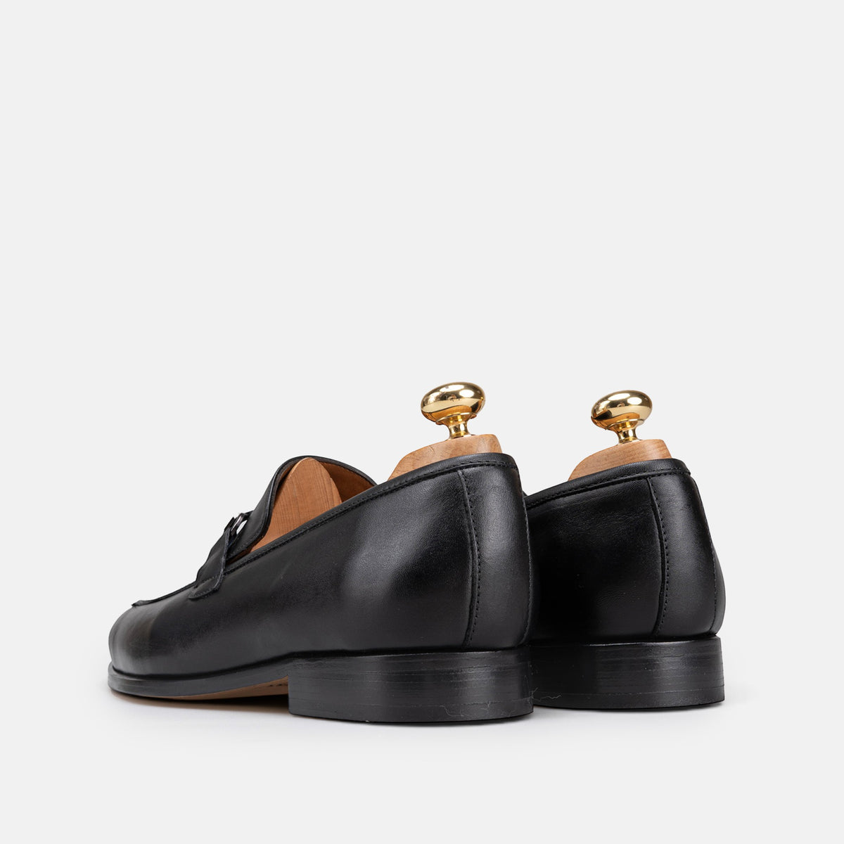 VOLZAK black leather loafers with wooden shoe trees, viewed from the back on a white background.