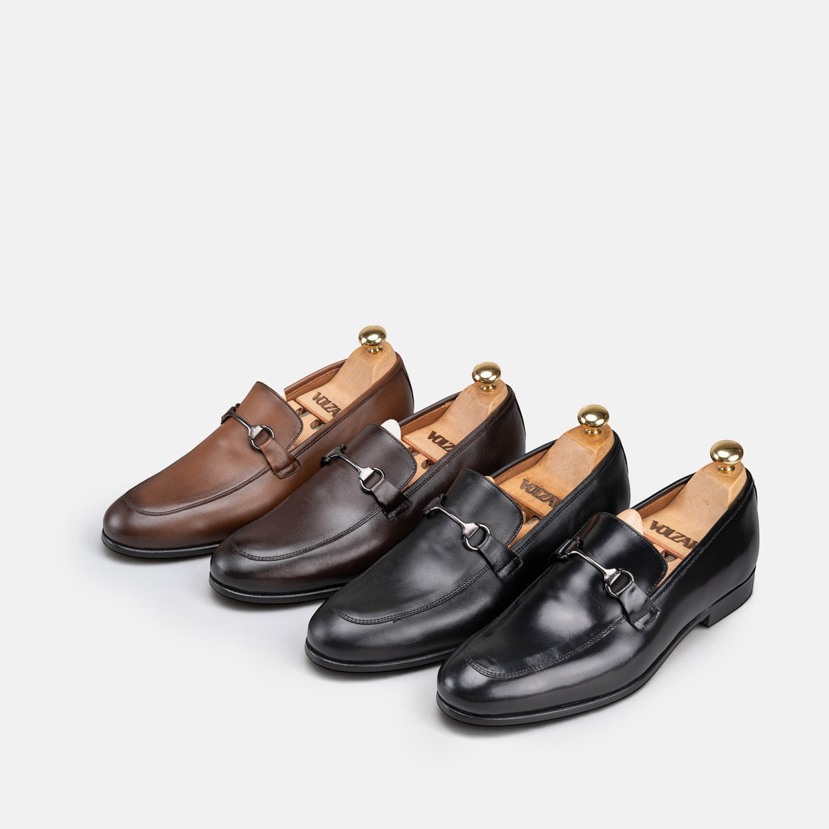VOLZAK leather loafers in brown and black with metal horsebit detail and wooden shoe trees on a white background
